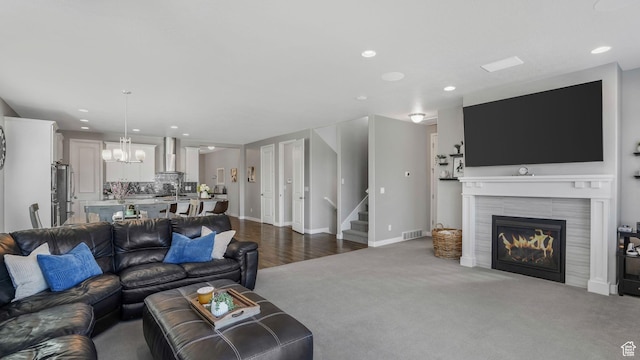living area featuring dark carpet, visible vents, a tiled fireplace, stairs, and a notable chandelier