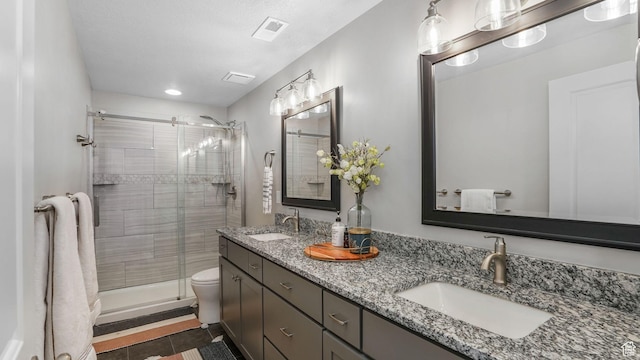 bathroom featuring toilet, double vanity, a sink, and a stall shower