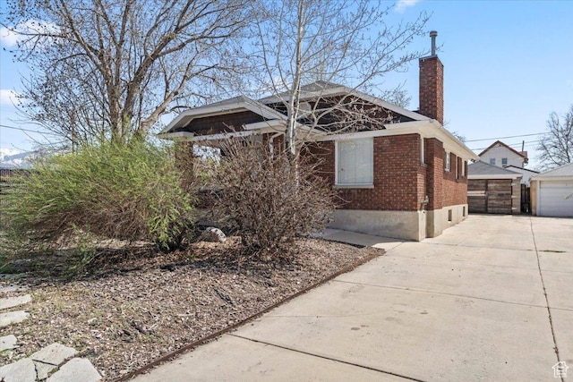 view of front facade with a chimney, a detached garage, an outdoor structure, and brick siding