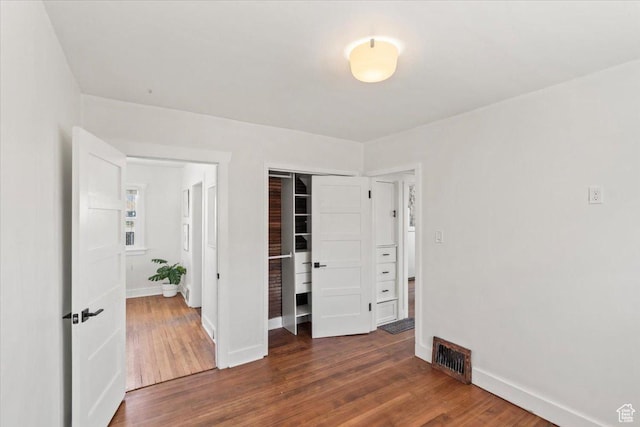 unfurnished bedroom with a closet, dark wood-style flooring, baseboards, and visible vents