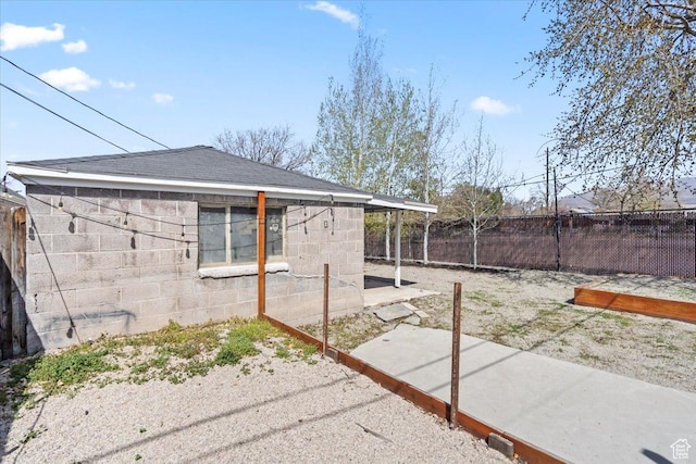 view of side of property featuring roof with shingles, concrete block siding, fence, and a patio