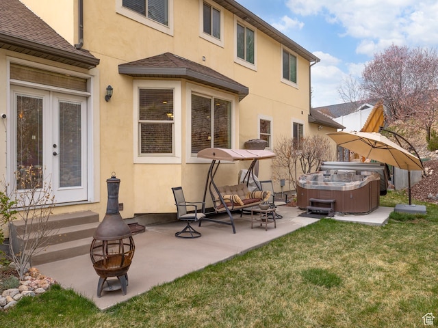 rear view of property with stucco siding, a patio area, an outdoor fire pit, a hot tub, and a yard