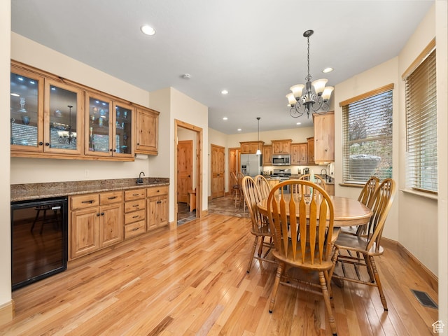 dining area with wine cooler, visible vents, an inviting chandelier, and light wood-style floors