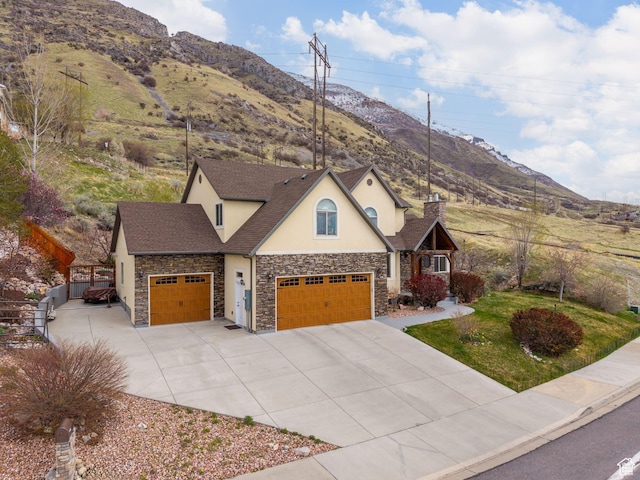 view of front facade featuring a mountain view, stone siding, a garage, concrete driveway, and stucco siding