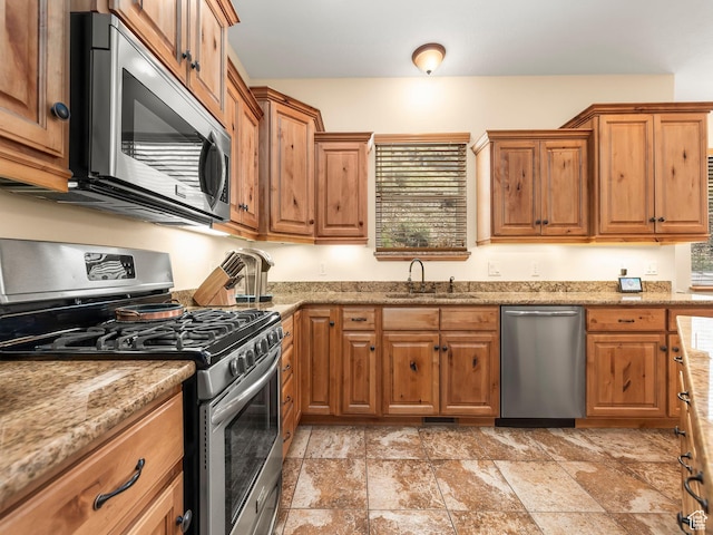 kitchen with a sink, stone finish flooring, brown cabinetry, and stainless steel appliances