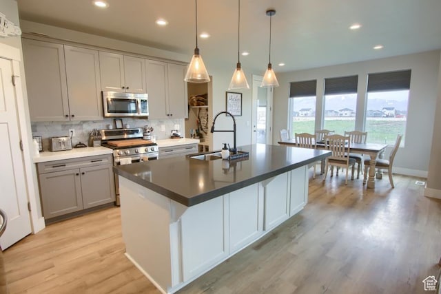 kitchen featuring a sink, light wood-type flooring, gray cabinetry, stainless steel appliances, and decorative backsplash