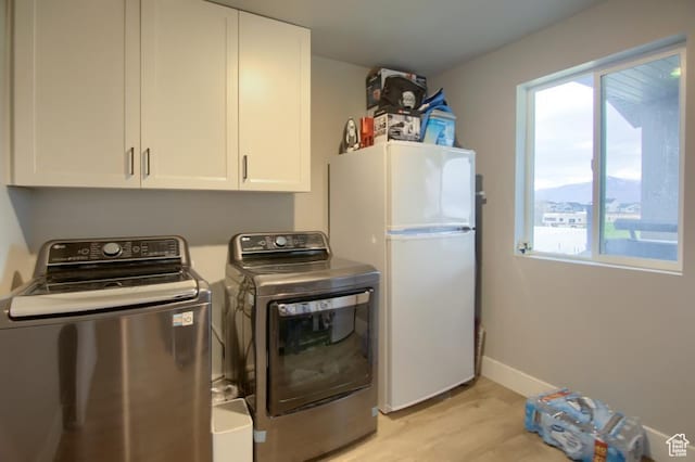 clothes washing area featuring cabinet space, baseboards, washer and dryer, and light wood-style floors
