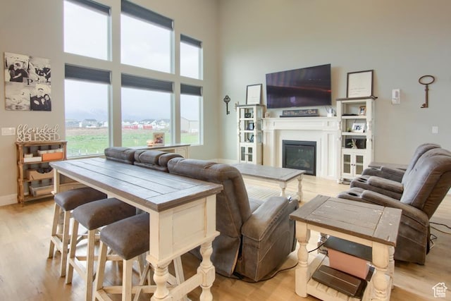 living area featuring a glass covered fireplace, light wood finished floors, a high ceiling, and baseboards