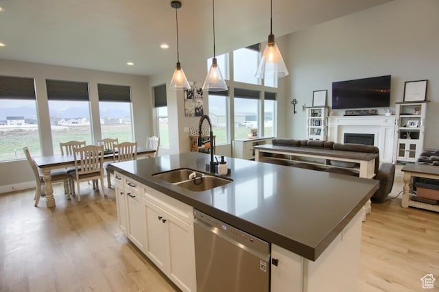 kitchen with open floor plan, dark countertops, light wood-style floors, dishwasher, and a sink