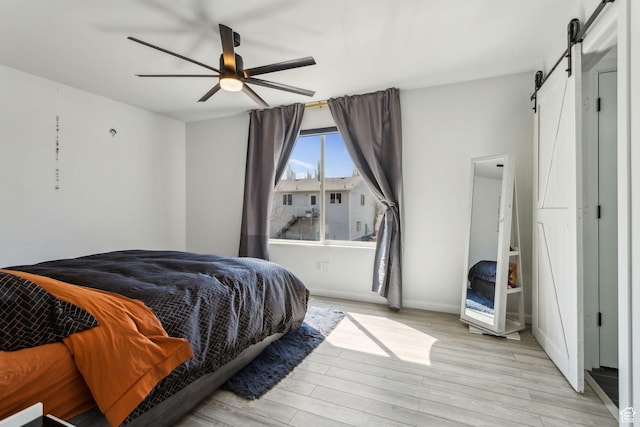 bedroom featuring light wood-type flooring, ceiling fan, and a barn door