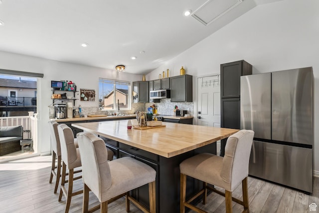 kitchen with stainless steel appliances, a breakfast bar area, backsplash, and lofted ceiling