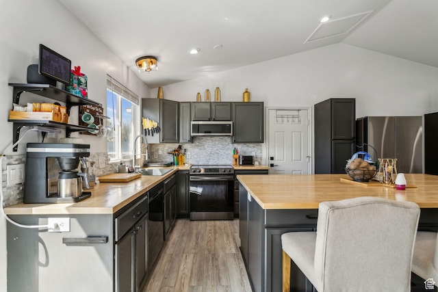 kitchen featuring a sink, backsplash, appliances with stainless steel finishes, and lofted ceiling