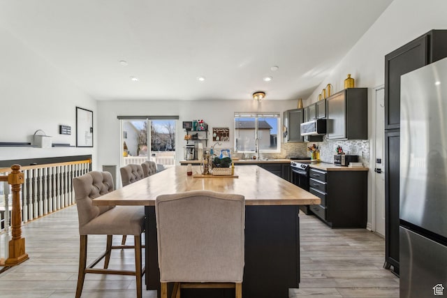 kitchen with a kitchen breakfast bar, tasteful backsplash, appliances with stainless steel finishes, wood counters, and light wood finished floors