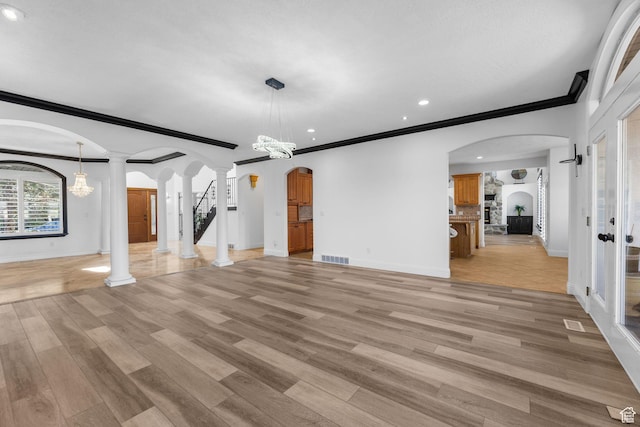 unfurnished living room with arched walkways, light wood-style floors, ornate columns, and baseboards