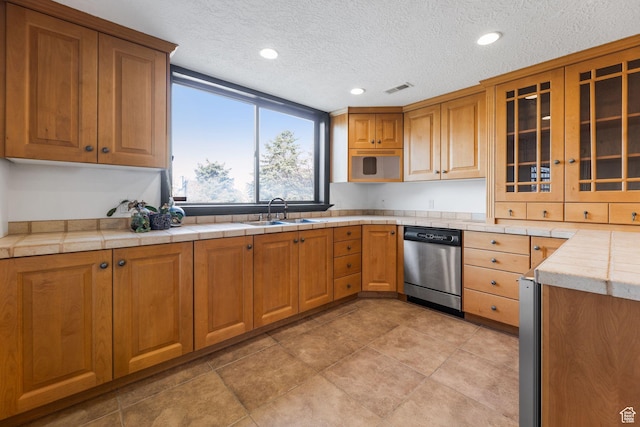 kitchen with visible vents, glass insert cabinets, a sink, brown cabinetry, and stainless steel dishwasher