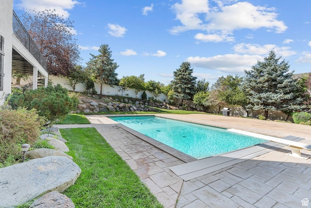 view of pool with a patio area, fence, a fenced in pool, and a diving board
