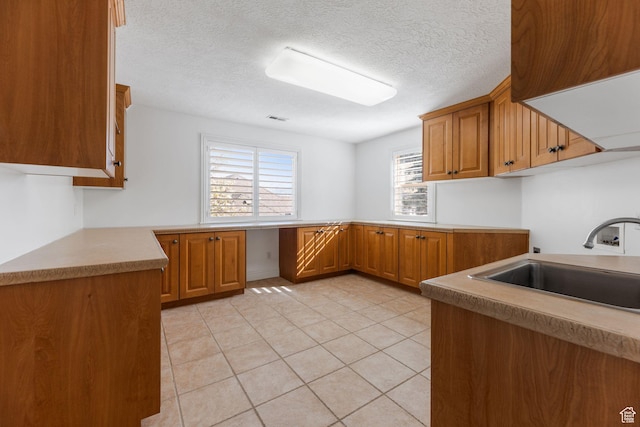 kitchen featuring light tile patterned floors, brown cabinets, a sink, and a textured ceiling