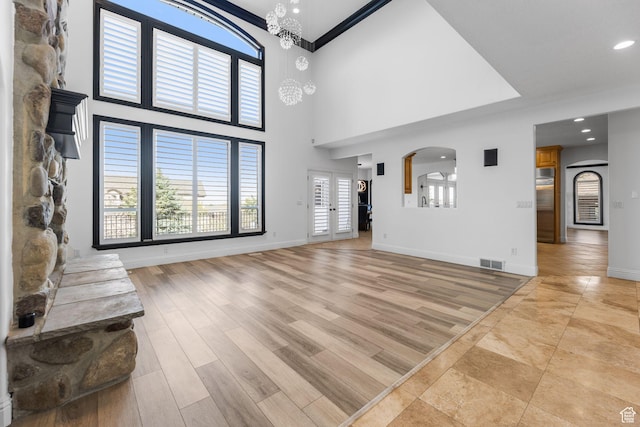 unfurnished living room with arched walkways, light wood finished floors, baseboards, and visible vents