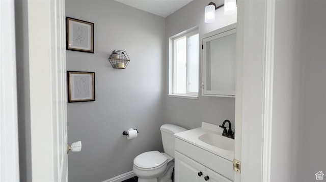 half bath with baseboards, vanity, and toilet