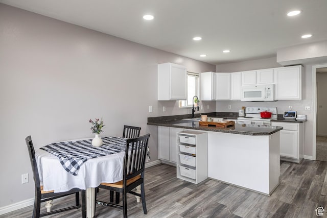 kitchen featuring a peninsula, a sink, white appliances, and baseboards