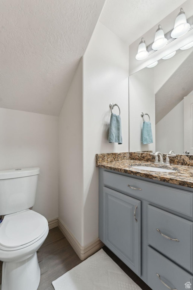 half bath with a textured ceiling, vanity, vaulted ceiling, toilet, and baseboards