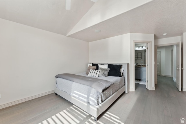 bedroom with ensuite bathroom, baseboards, vaulted ceiling, and wood finished floors