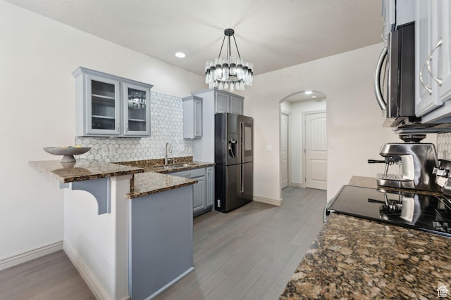 kitchen featuring glass insert cabinets, a peninsula, arched walkways, black fridge, and a sink