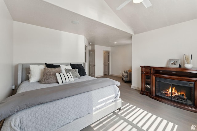 bedroom featuring baseboards, a warm lit fireplace, a ceiling fan, lofted ceiling, and wood finished floors