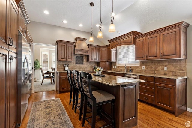 kitchen featuring a center island, decorative light fixtures, premium range hood, a kitchen bar, and wood finished floors
