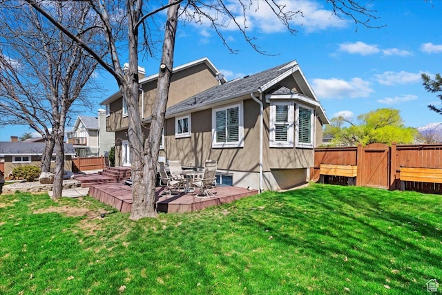 rear view of house with fence, a gate, a lawn, and stucco siding