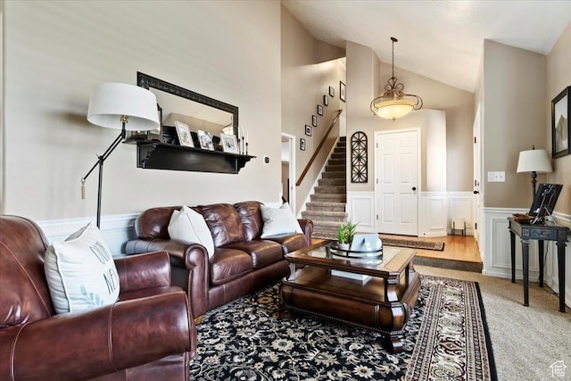 living area featuring a decorative wall, carpet, stairway, wainscoting, and lofted ceiling