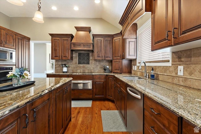kitchen with custom range hood, a warming drawer, appliances with stainless steel finishes, light wood finished floors, and a sink