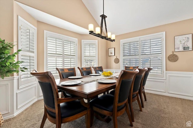 dining room with a decorative wall, light colored carpet, vaulted ceiling, wainscoting, and a notable chandelier