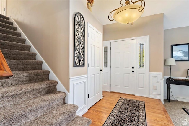 entrance foyer featuring light wood-style flooring, a decorative wall, wainscoting, and stairs