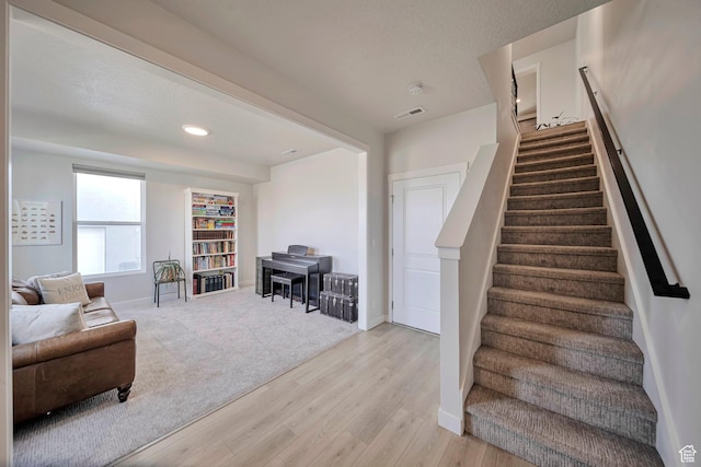 interior space with baseboards, a textured ceiling, stairs, visible vents, and light wood finished floors