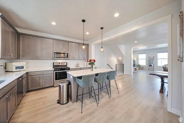 kitchen featuring a kitchen breakfast bar, open floor plan, light countertops, light wood-style floors, and stainless steel appliances