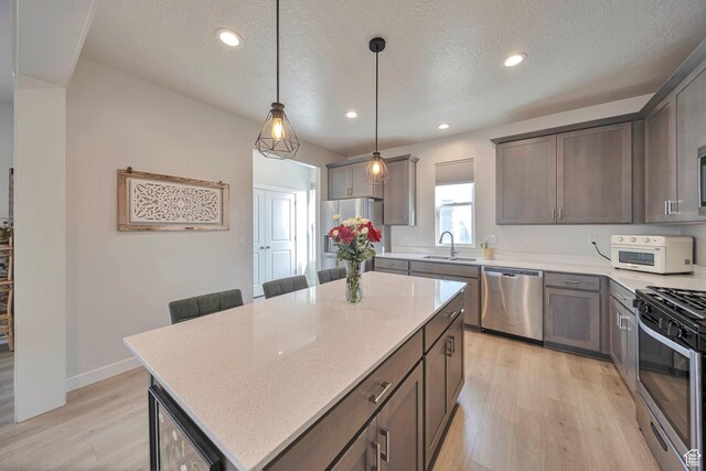kitchen featuring stainless steel appliances, light stone countertops, light wood-style floors, and a sink