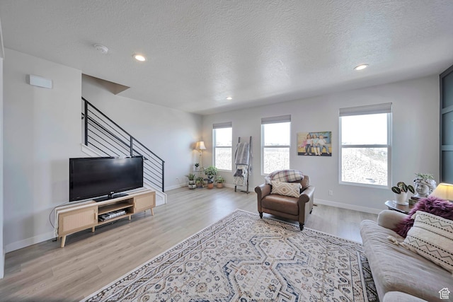 living room with baseboards, a textured ceiling, light wood finished floors, recessed lighting, and stairs