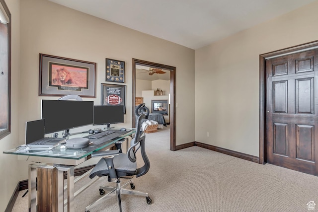 carpeted office space featuring baseboards, ceiling fan, and a fireplace
