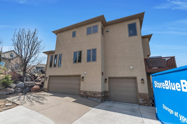 back of property featuring an attached garage, driveway, stucco siding, and stone siding