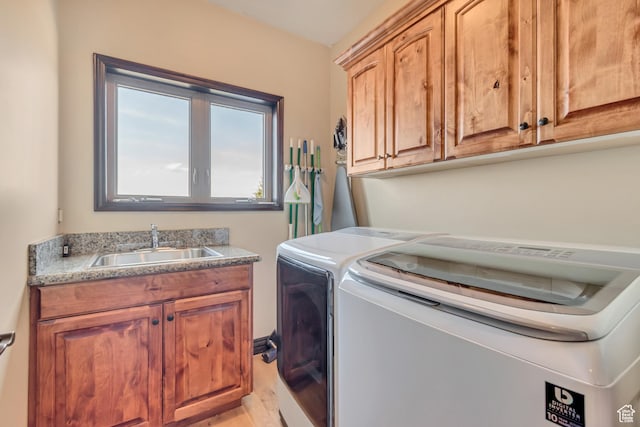 clothes washing area with light wood finished floors, washing machine and clothes dryer, a sink, and cabinet space