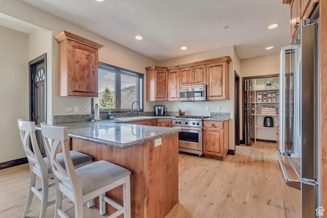 kitchen with a peninsula, light wood-style flooring, a breakfast bar, and high quality appliances