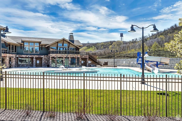 pool with fence, a water slide, a patio, and a lawn