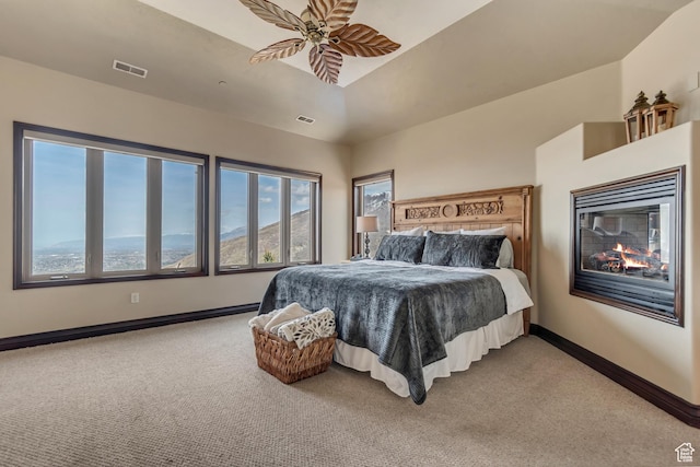 carpeted bedroom with a multi sided fireplace, ceiling fan, baseboards, and visible vents