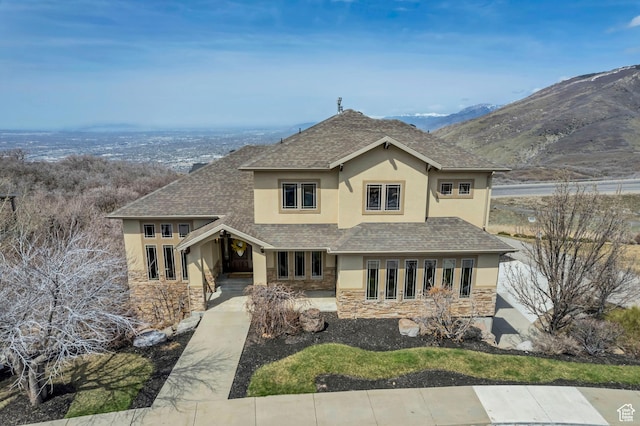 view of front facade with a shingled roof, stucco siding, and stone siding