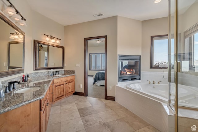 full bathroom with visible vents, a sink, double vanity, a glass covered fireplace, and a garden tub