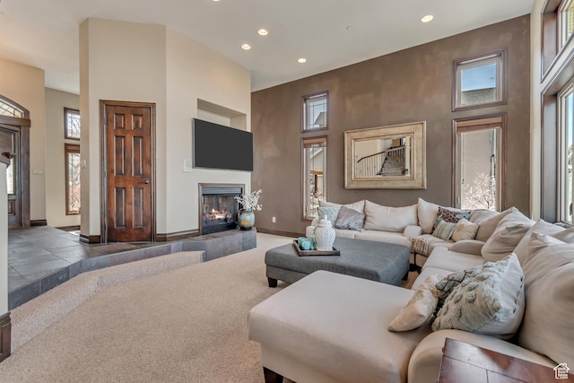 living area featuring a lit fireplace, a towering ceiling, baseboards, and recessed lighting