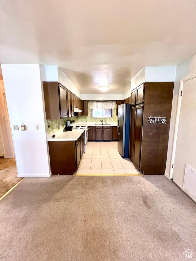 kitchen featuring light countertops, freestanding refrigerator, dark brown cabinets, electric stove, and light colored carpet