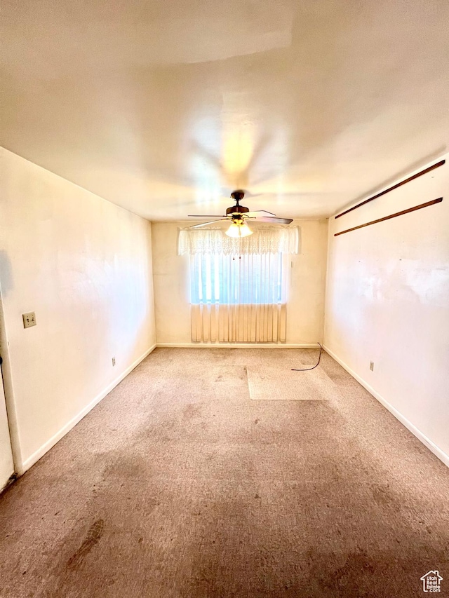 carpeted spare room featuring baseboards and a ceiling fan