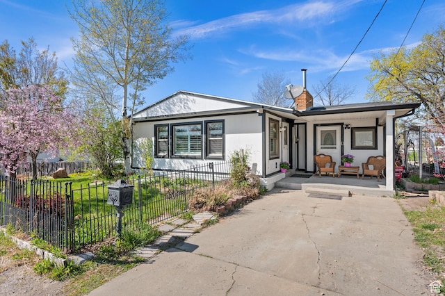 bungalow-style house featuring covered porch, a chimney, a front lawn, and a fenced front yard